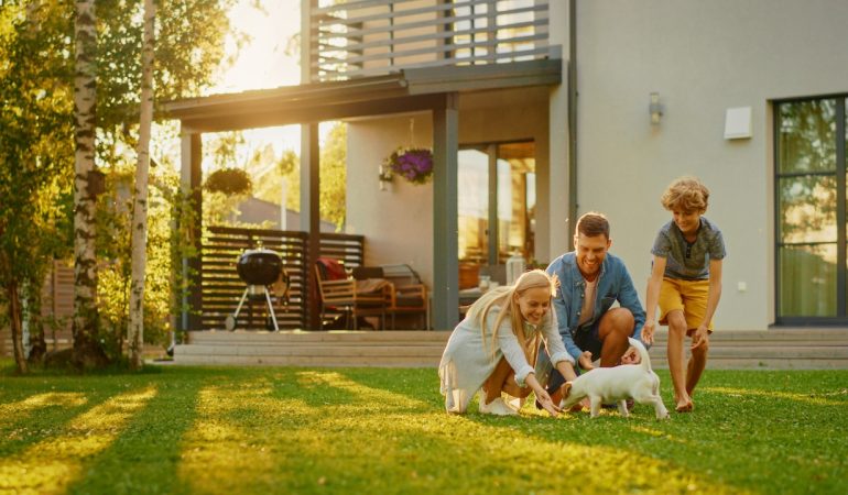 Smiling Father, Mother and Son Pet and Play with Smooth Fox Terrier Retriever Dog. Sun Shines on Idyllic Happy Family with Loyal Pedigree Dog have Fun at the Idyllic Suburban House Backyard